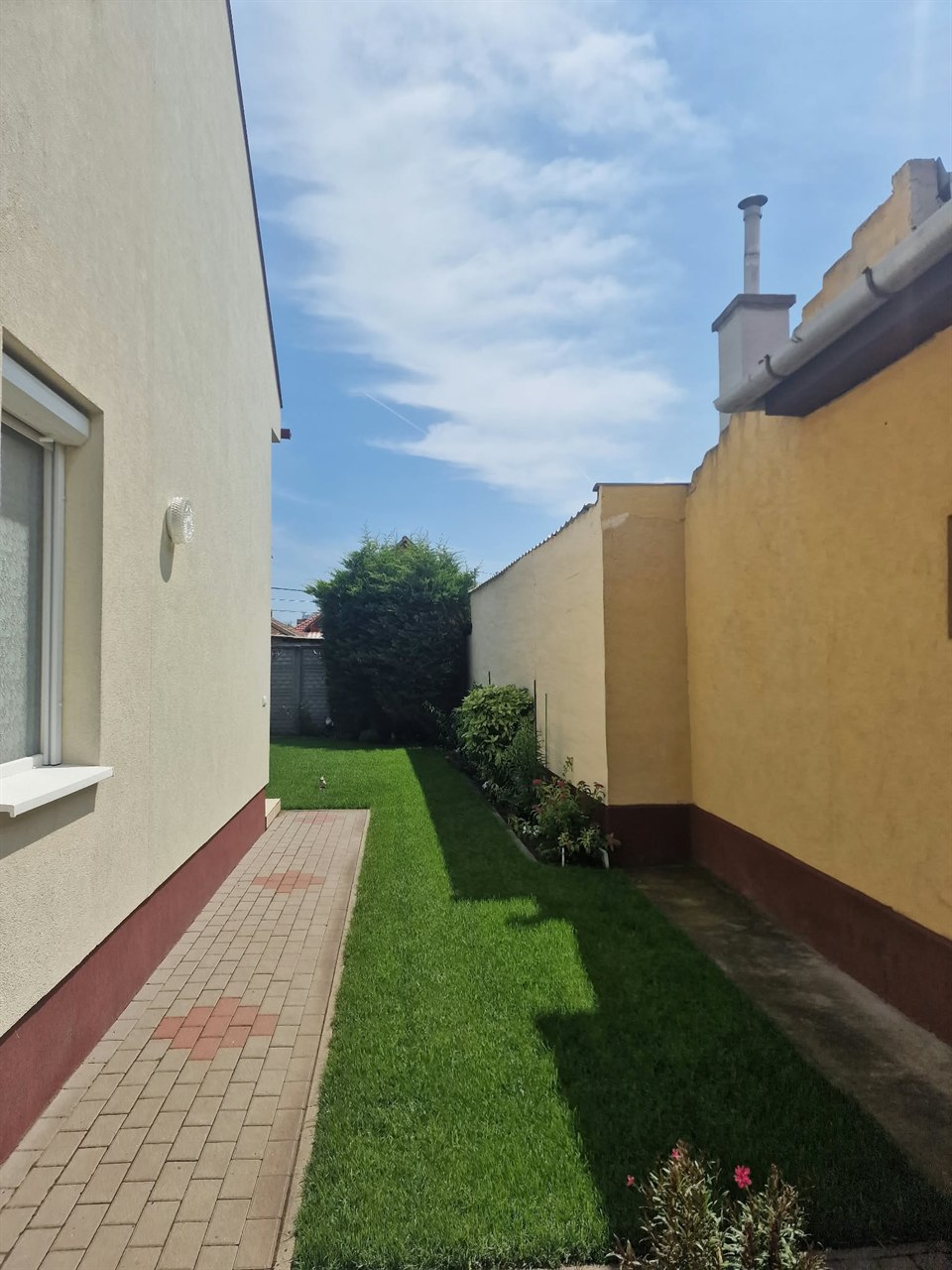Ugyanaz a keskeny kertsáv gyeppel a ház és a szomszéd fal között